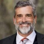 A man with grey hair and beard wearing a suit.